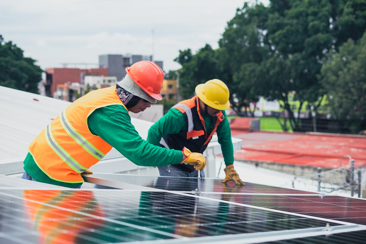 hero-homepage Two workers installing rooftop solar panels safely equipped with PPE and tools.